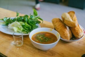 A bowl of flavorful Vietnamese soup accompanied by fresh greens and crusty baguette.